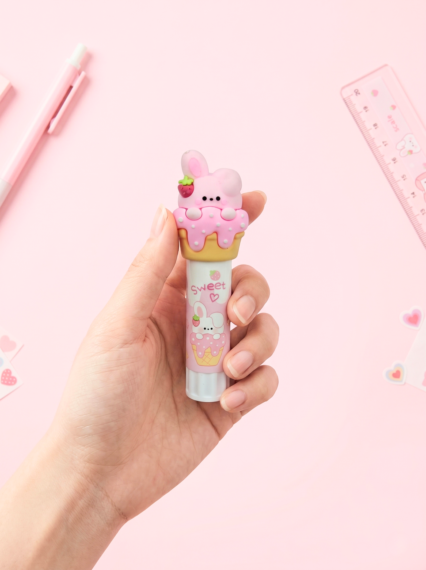 Hand holding a cute, cartoonish pink lip balm with a pink background