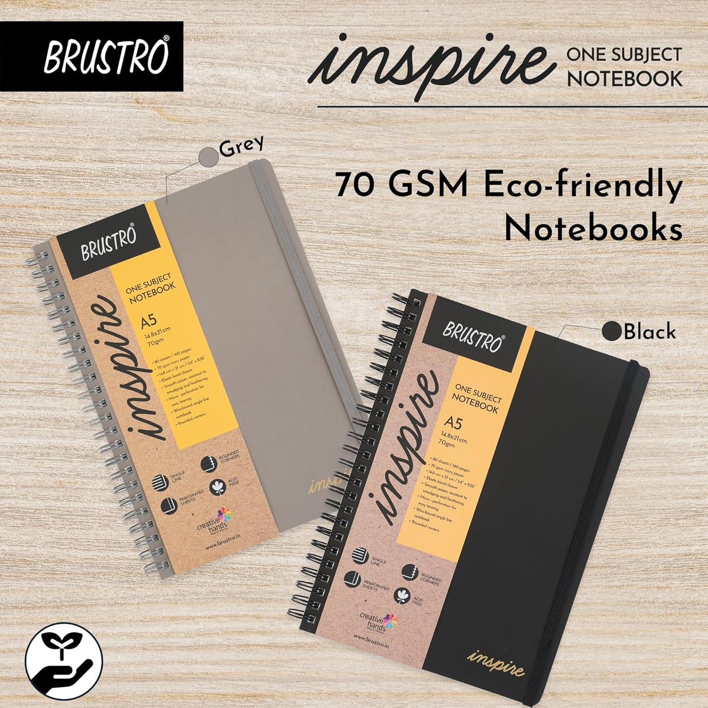 Two Brustro 'inspire' notebooks, one grey and one black, on a wooden surface.