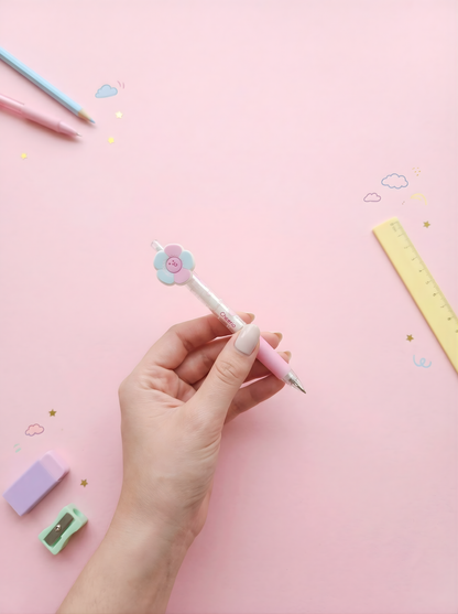 Hand holding a pink pen with a flower design on a pink background with stationery items.
