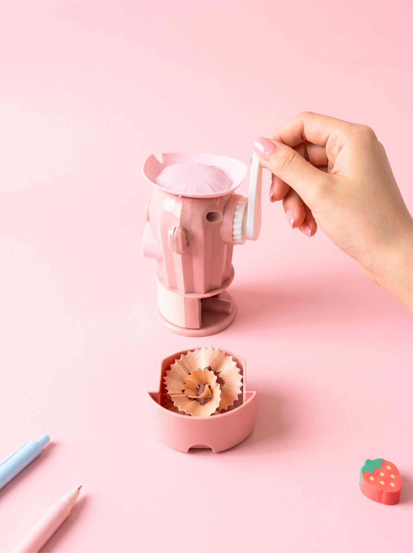 Pink pencil sharpener with a hand using it on a pink background