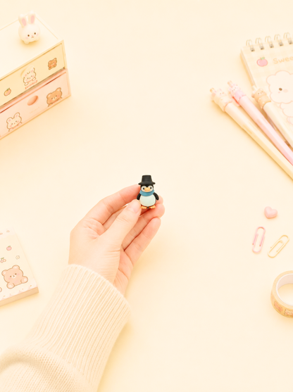 Small penguin figurine held by a hand on a light yellow background with stationery items.
