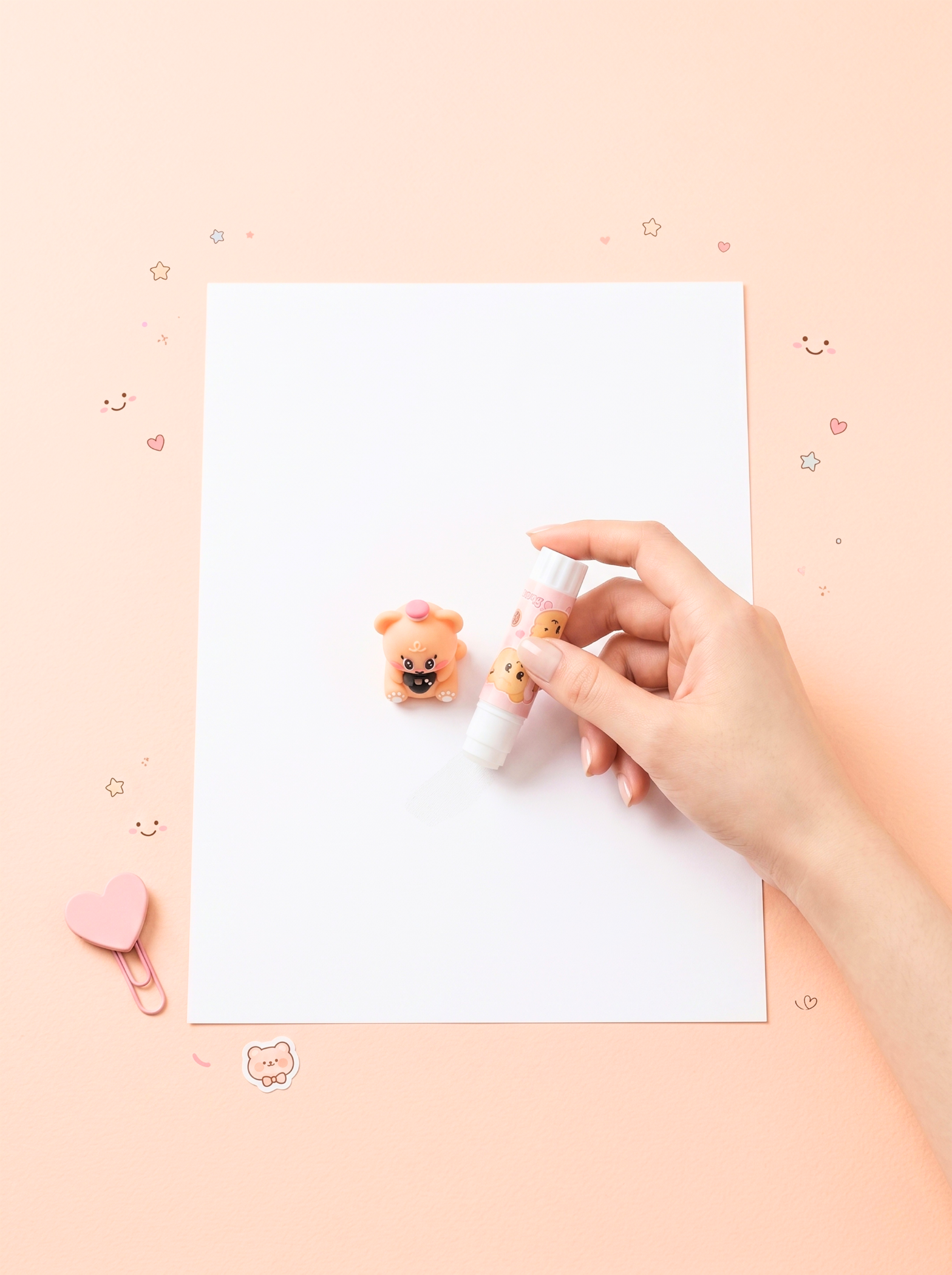 Hand holding a small pink toy with a bear design on a white sheet of paper against a light pink background.