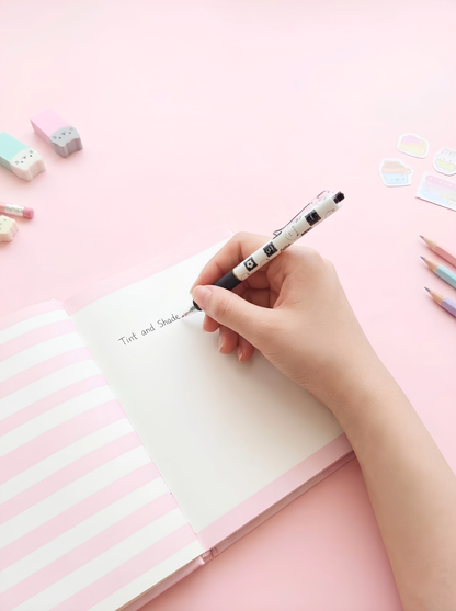 Hand writing on a pink and white striped notebook with stationery items on a pink background