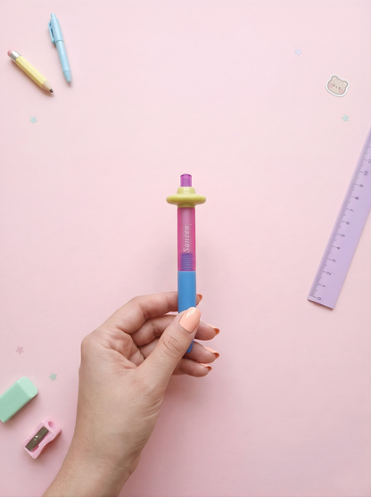 Colorful pen held by a hand on a pink background with stationery items.