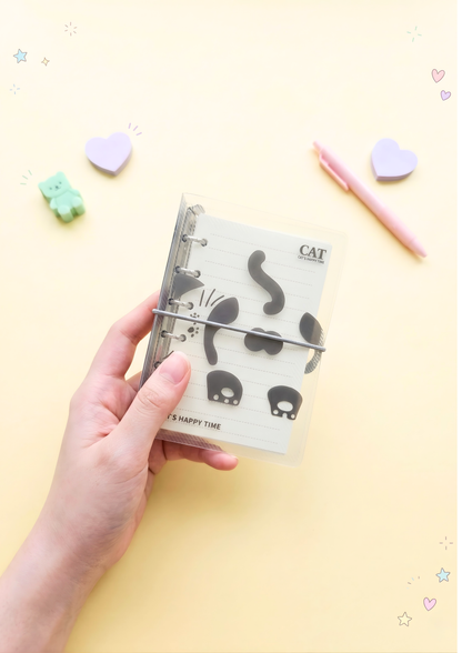 Hand holding a small notebook with cat illustrations on a yellow background
