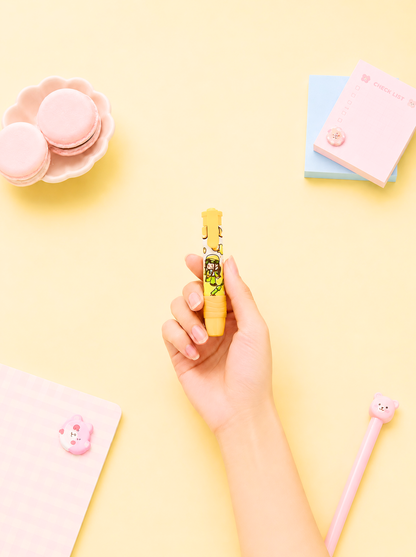Hand holding a yellow pen with a pink character on a pastel yellow background
