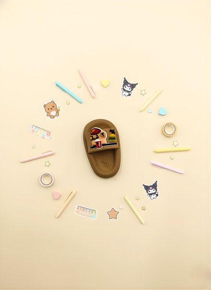 Brown sandal with cartoon character surrounded by colorful stationery items on a beige background