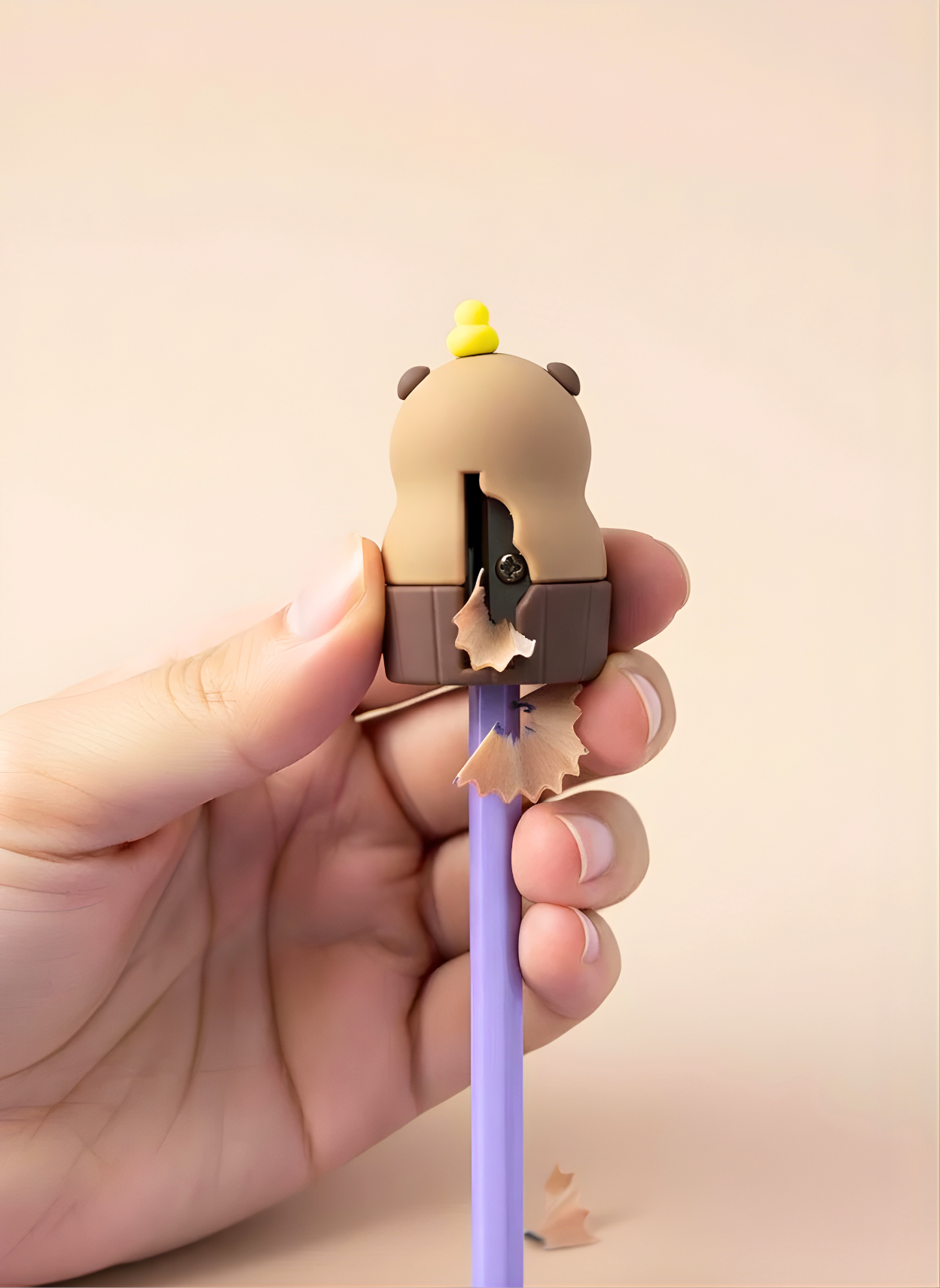 Pencil sharpener shaped like a cartoon character held by a hand with a beige background