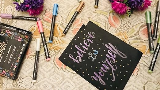 Colorful markers and a card with 'believe in yourself' text on a patterned surface.