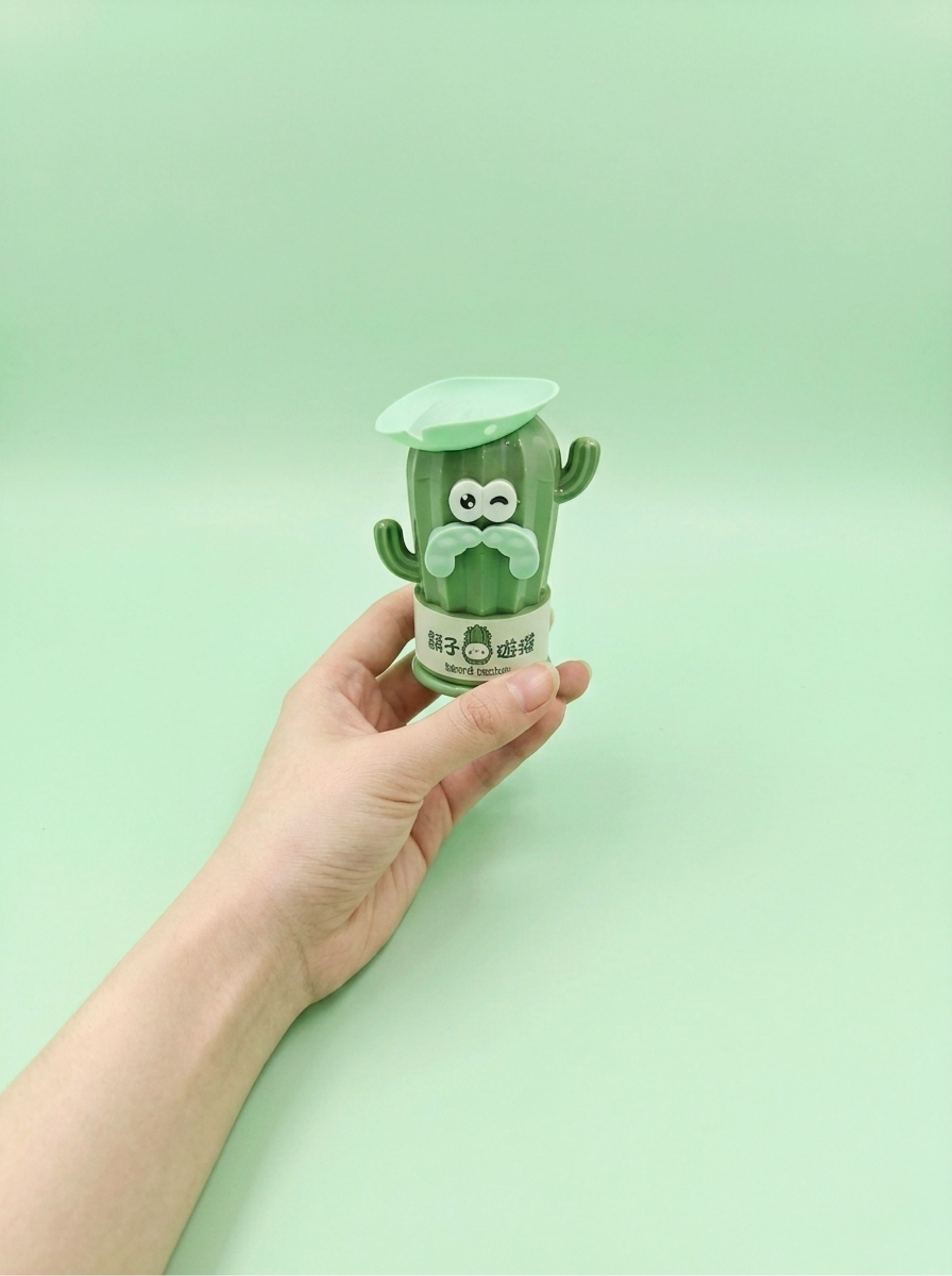 Hand holding a green cactus-shaped container against a light green background