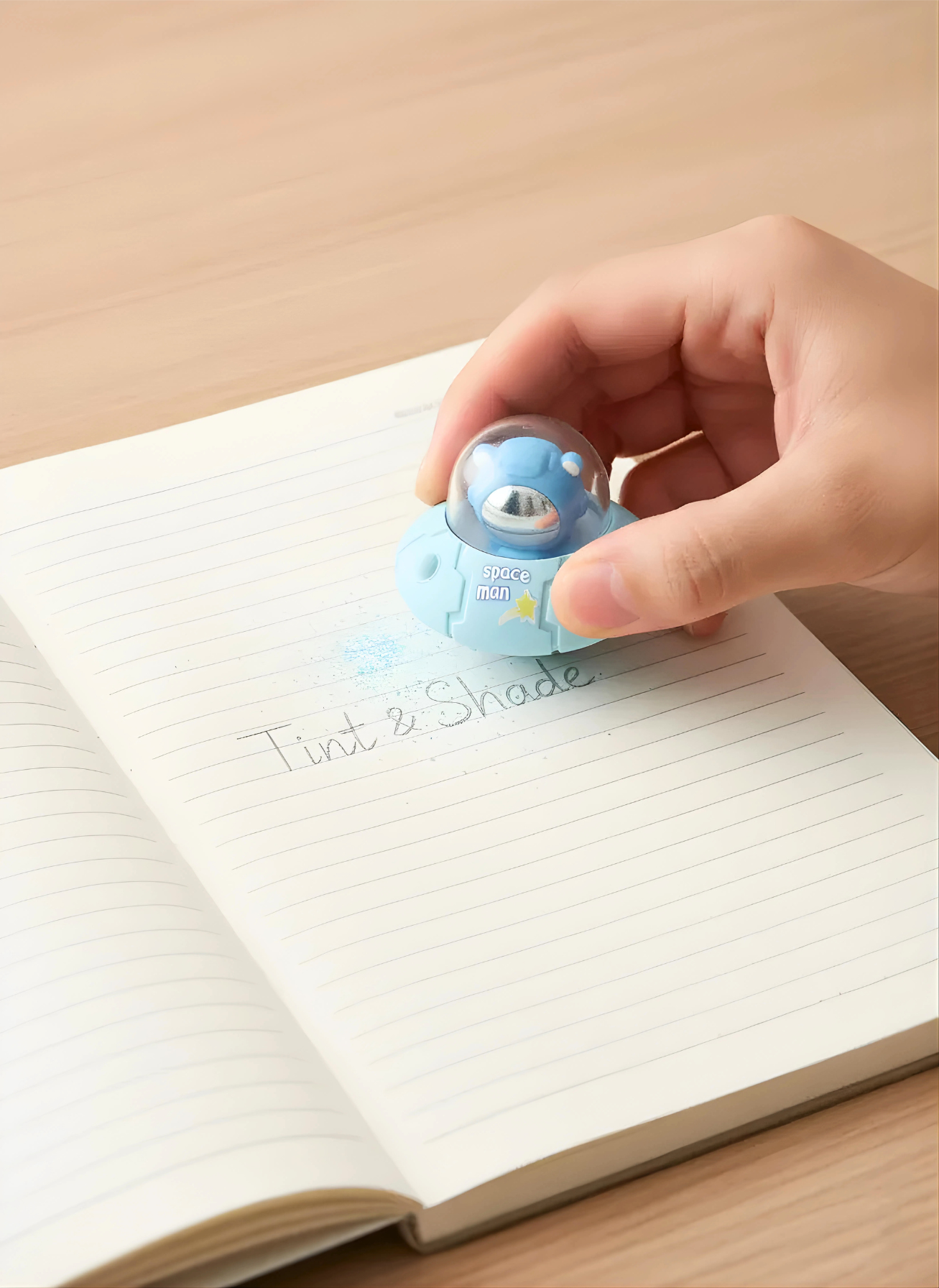 Hand holding a small blue object over an open notebook on a wooden surface