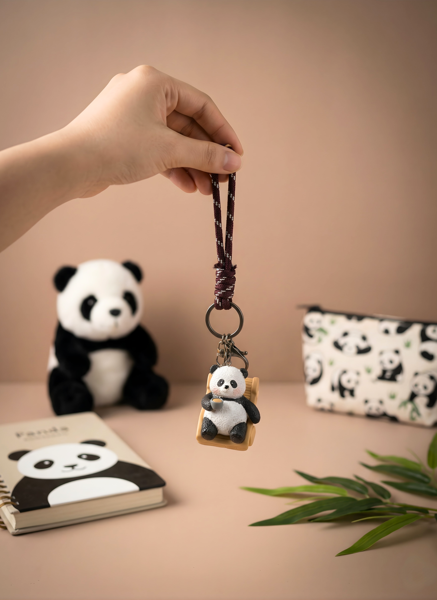Panda keychain held by a hand with a panda-themed notebook and pouch in the background.