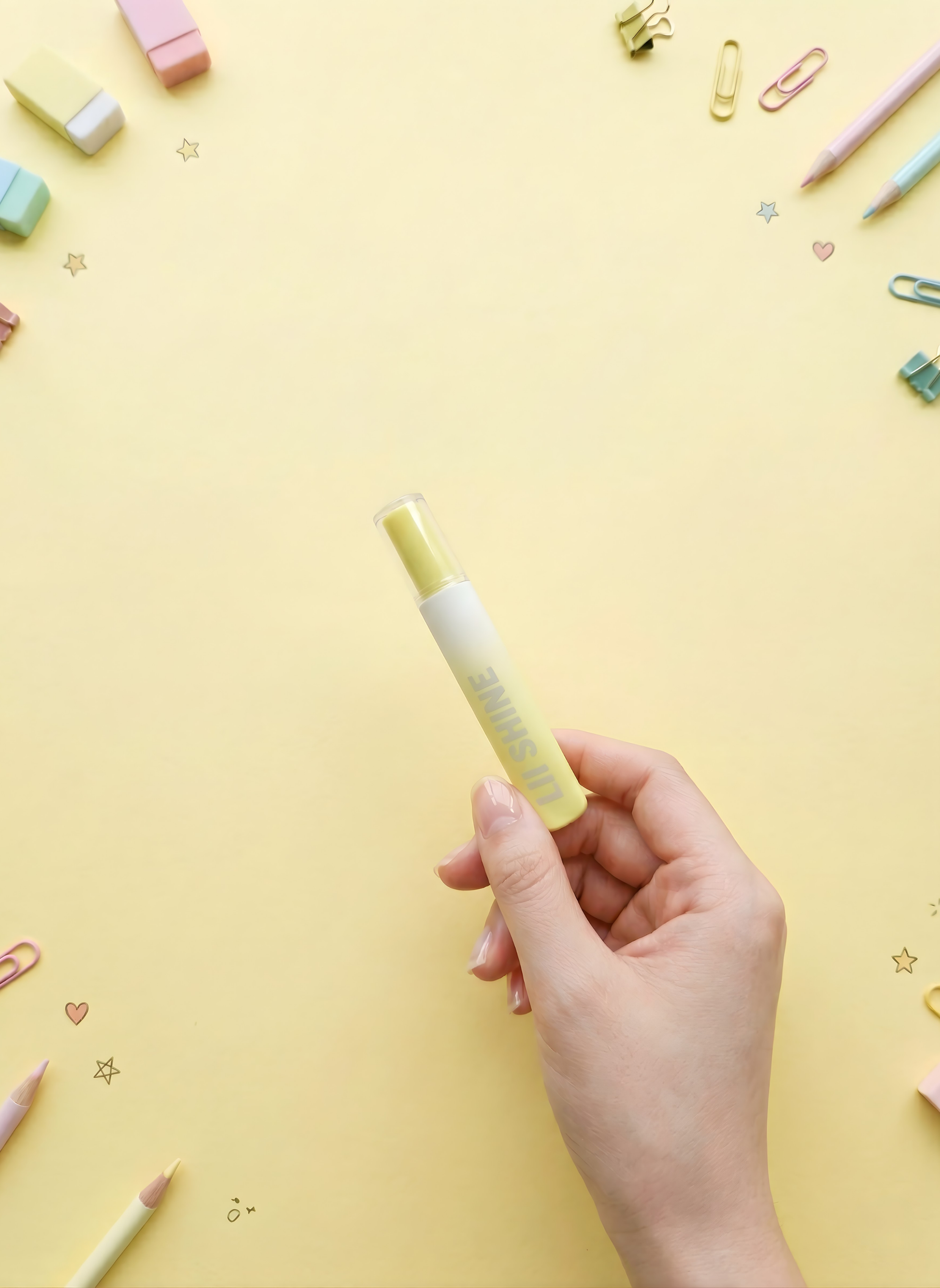 Hand holding a yellow highlighter pen on a yellow background with stationery items.