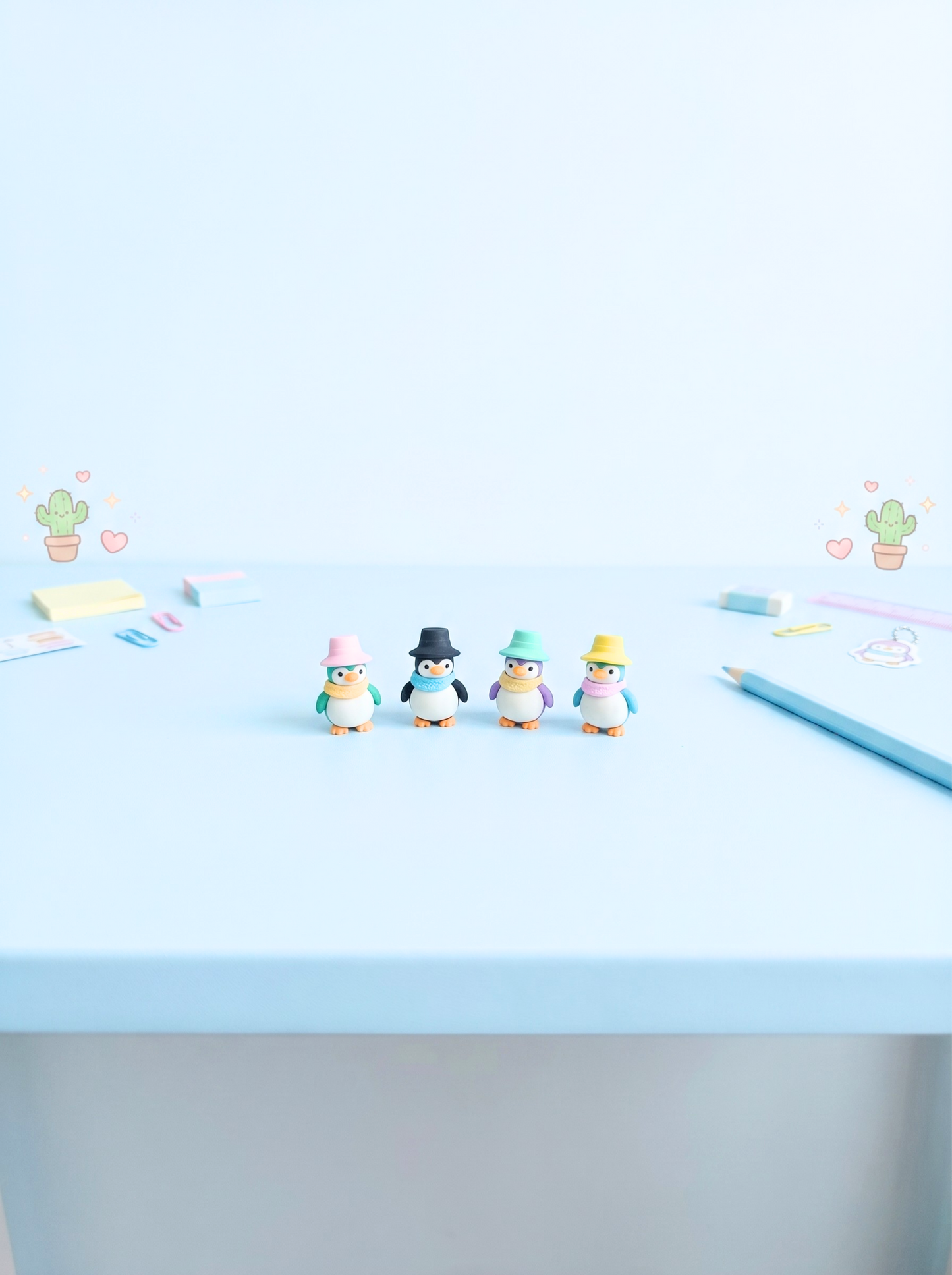 Small penguin figurines with hats on a light blue surface with scattered stationery items.