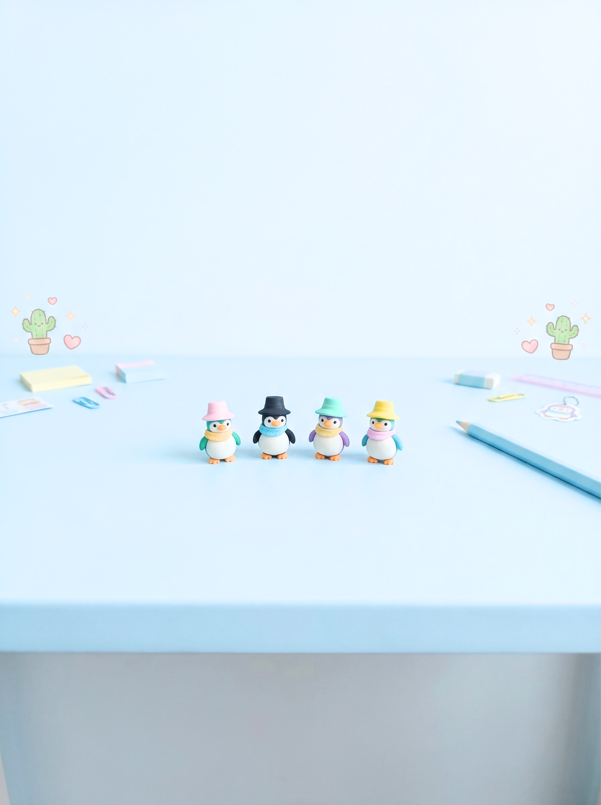 Small penguin figurines with hats on a light blue surface with scattered stationery items.