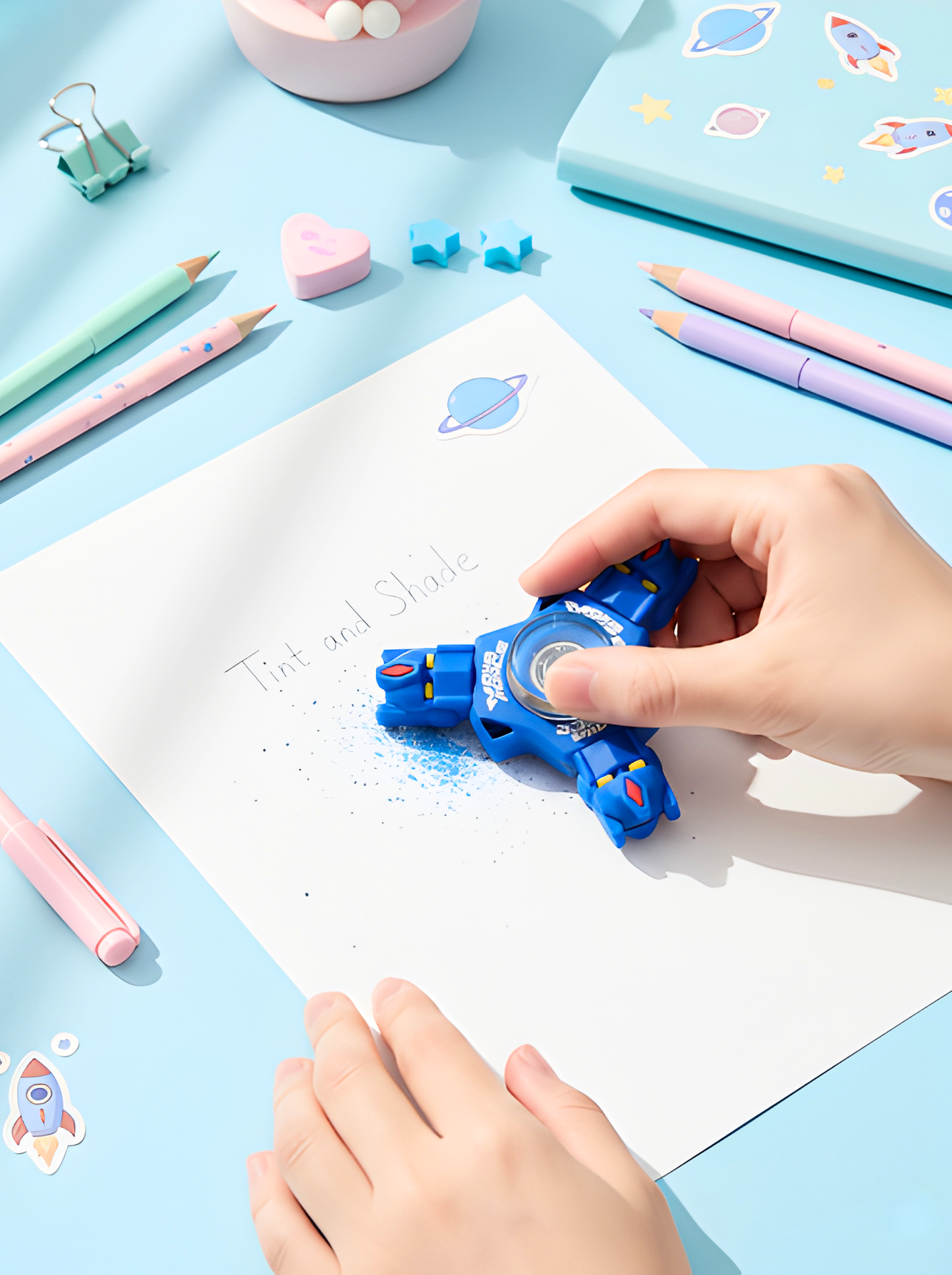 Child using a blue rocket-shaped eraser on a piece of paper with stationery items around.