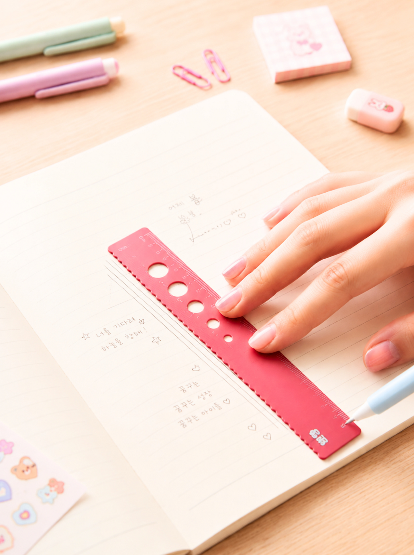 Hand using a red ruler on a notebook with stationery items in the background