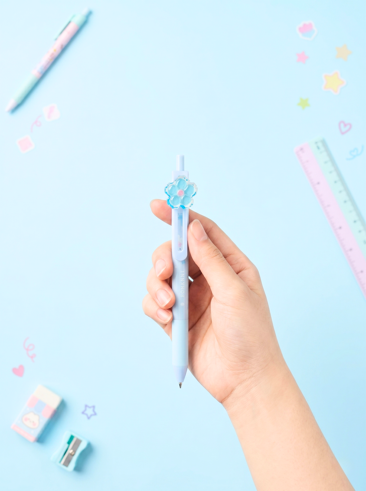 Hand holding a light blue pen with decorative elements on a light blue background