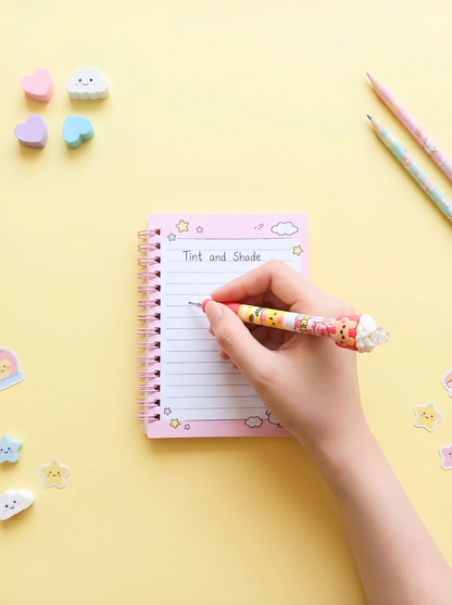 Hand holding a pen over a small notebook with colorful stickers on a yellow background