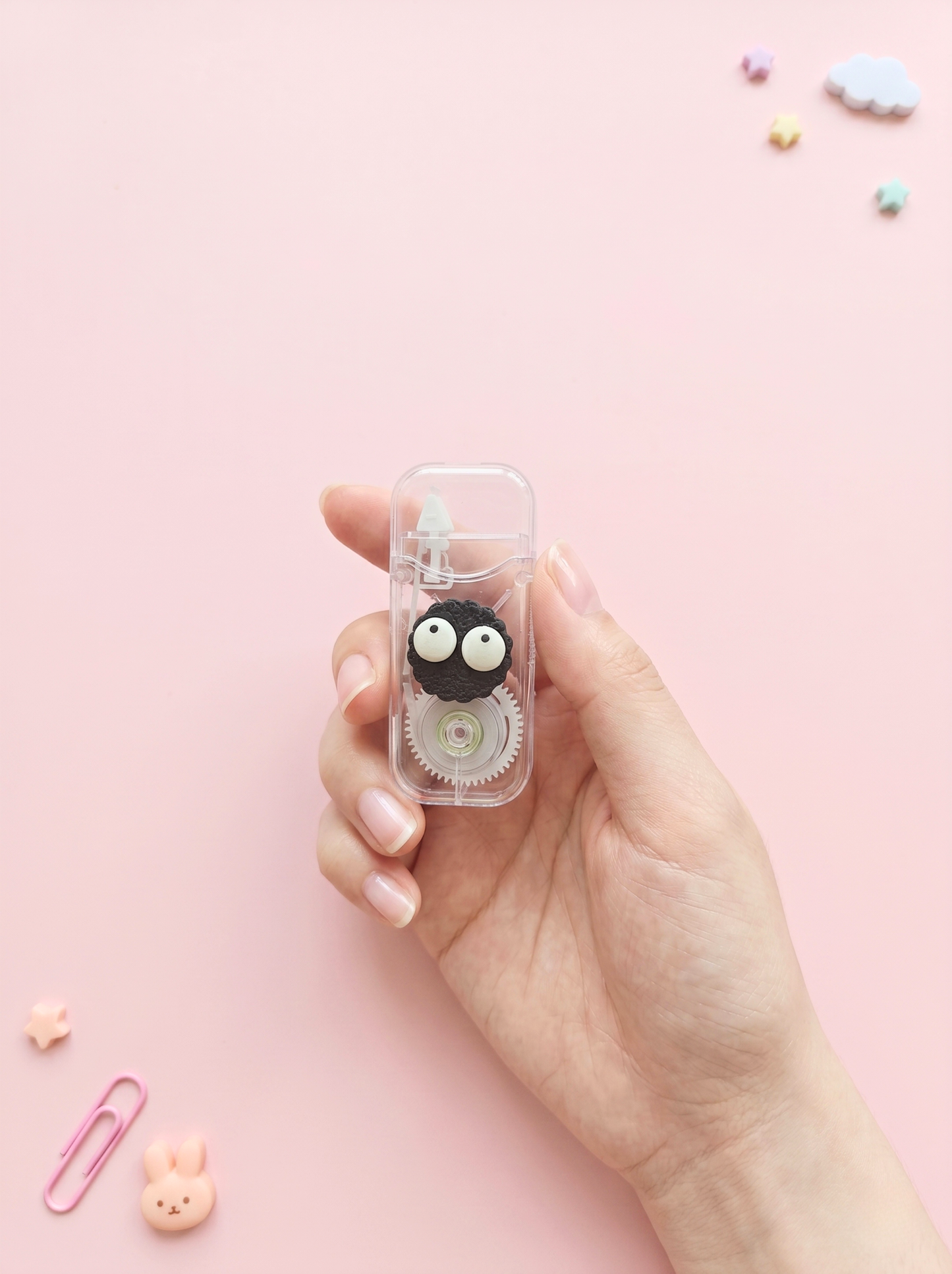 Hand holding a small transparent case with a black and white character on a pink background