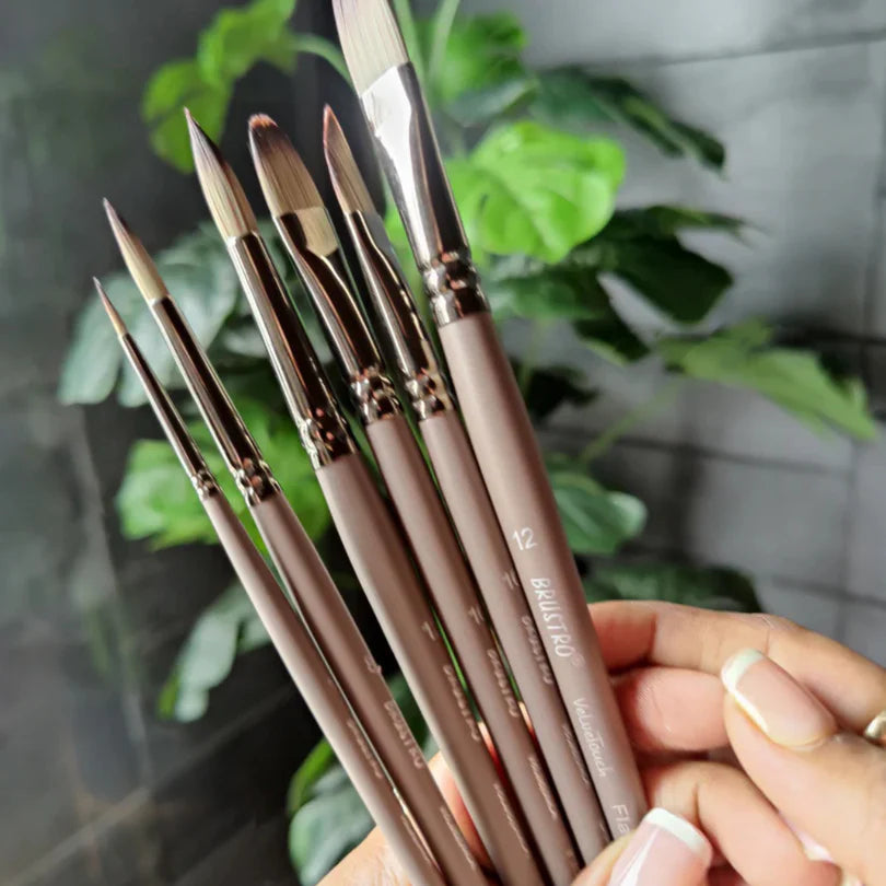 Set of paintbrushes held by a hand with a blurred green plant background