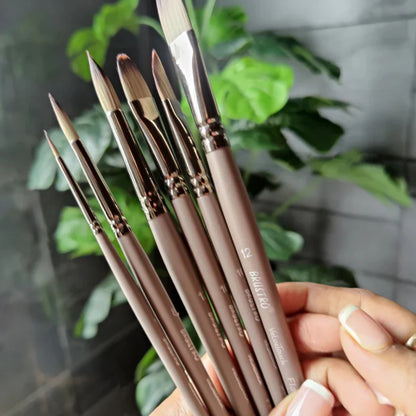 Set of paintbrushes held by a hand with a blurred green plant background