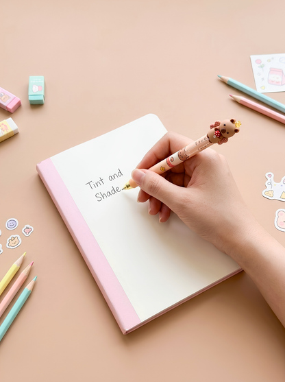 Hand holding a cute pen over a notebook with stationery items on a pink background