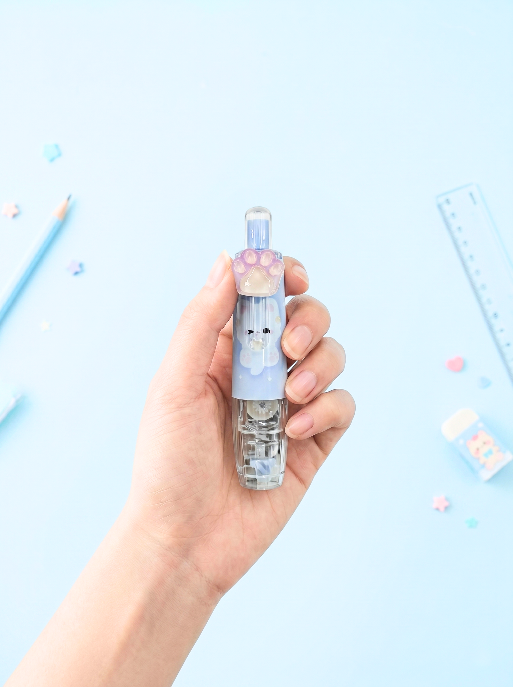 Hand holding a small transparent container with a blue lid featuring a cartoon face on a light blue background.