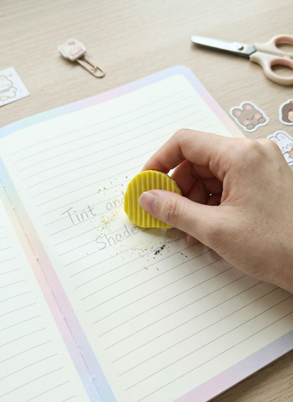 Hand using a yellow eraser on a notebook with stationery items in the background