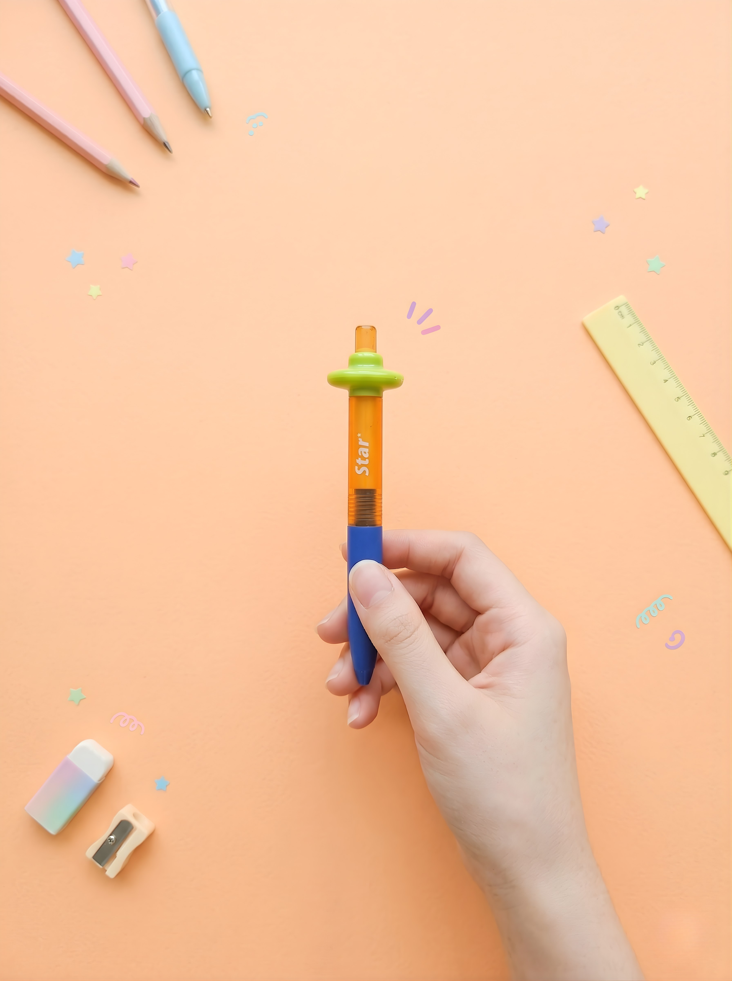 Hand holding a colorful pen with stationery items on a peach background