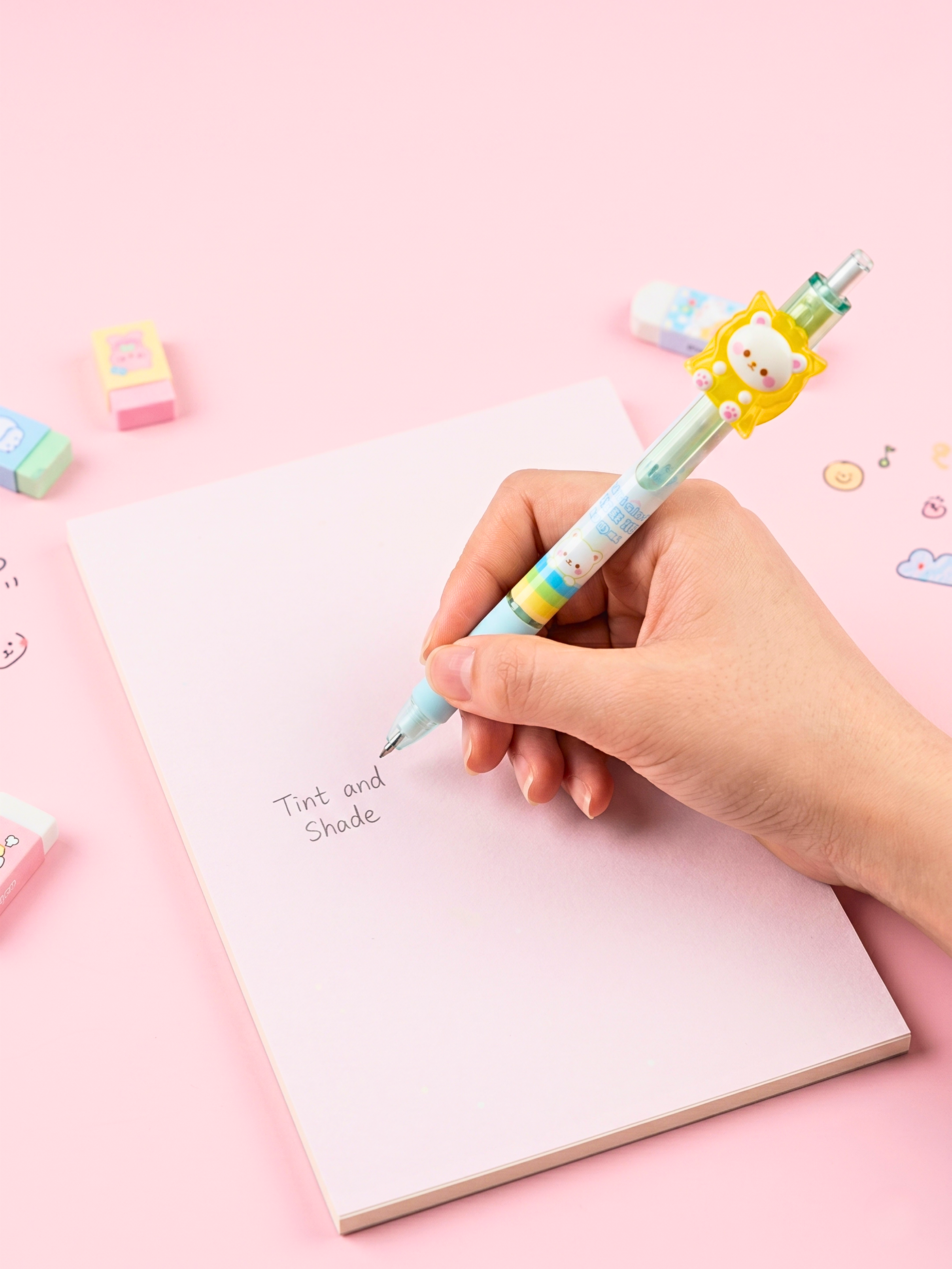 Hand holding a colorful pen over a notebook with a pink background