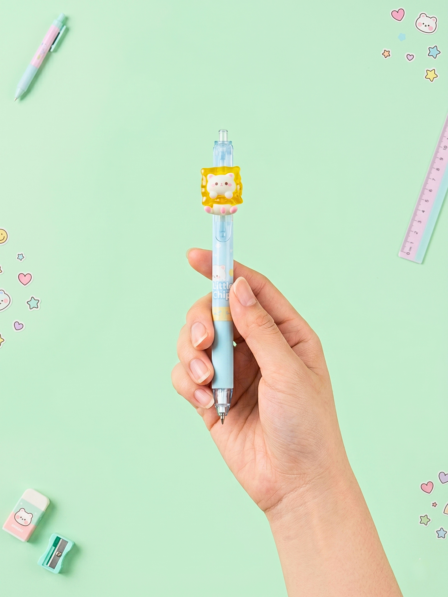 Hand holding a small blue pen with a cat-shaped clip on a light green background