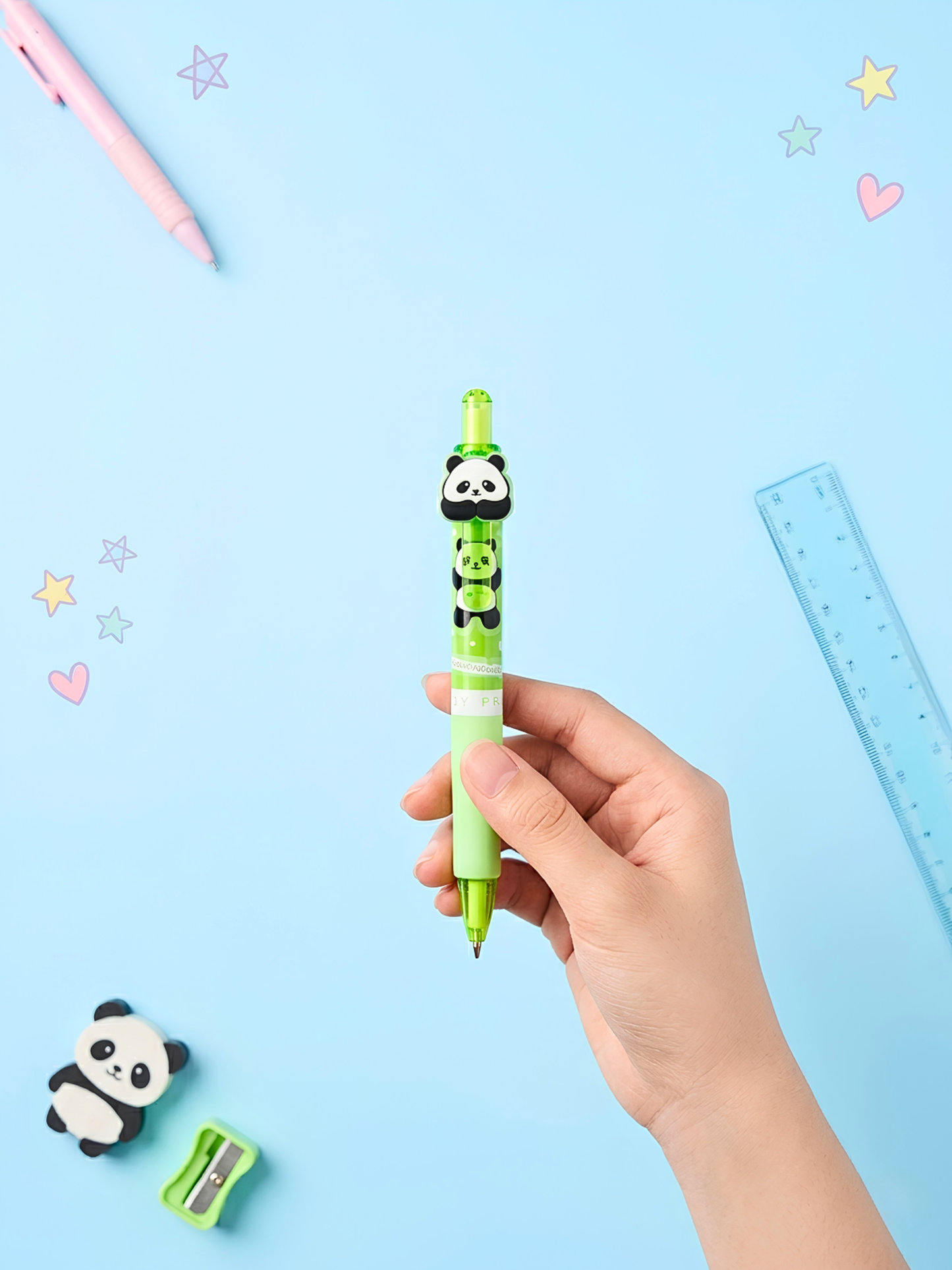 Hand holding a green panda-themed pen with stationery items on a light blue background