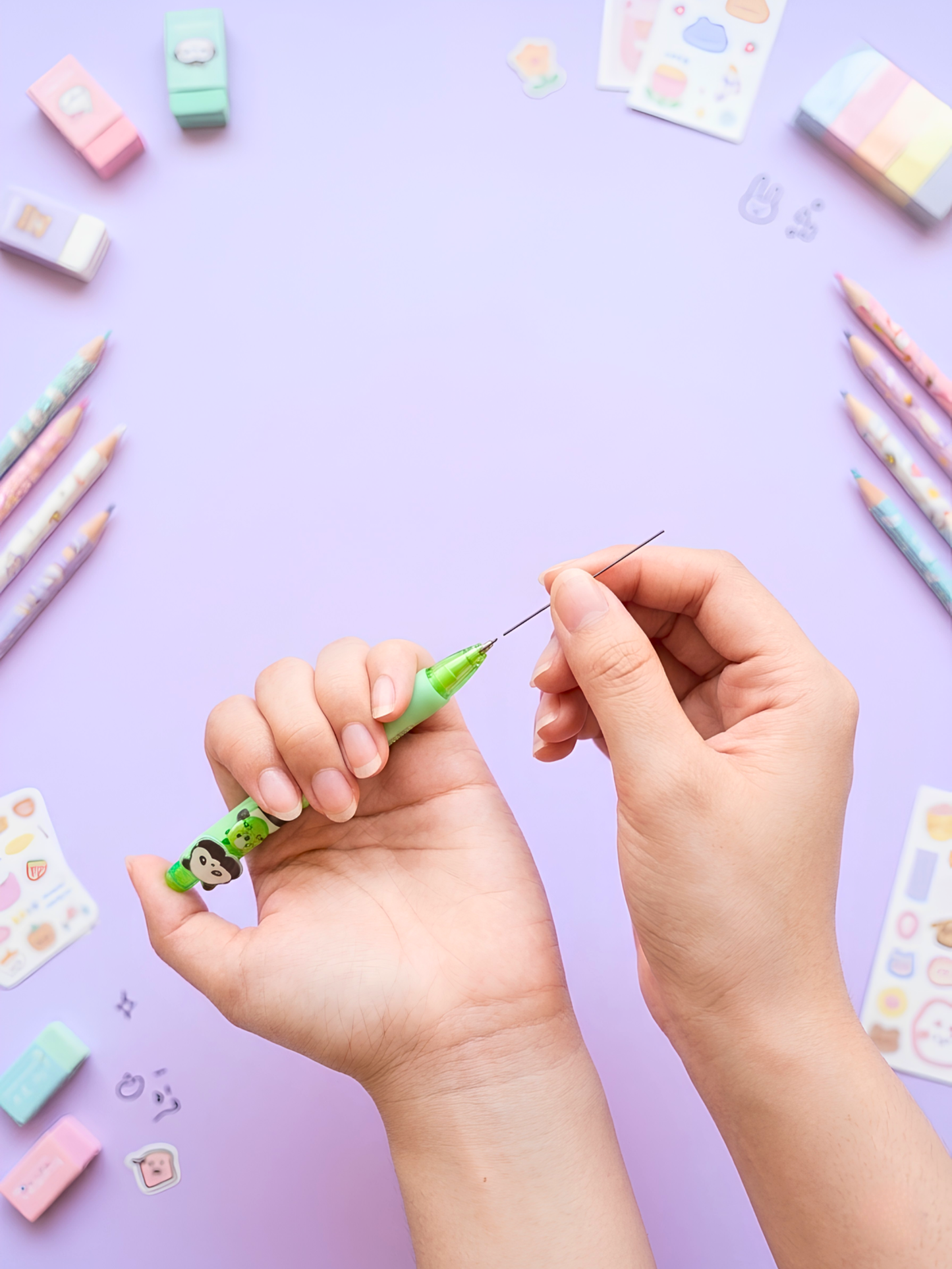 Hands holding a small green object with colorful stationery items on a purple background