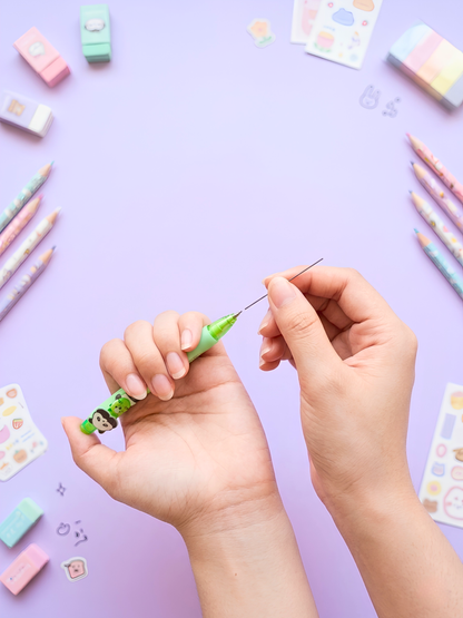 Hands holding a small green object with colorful stationery items on a purple background