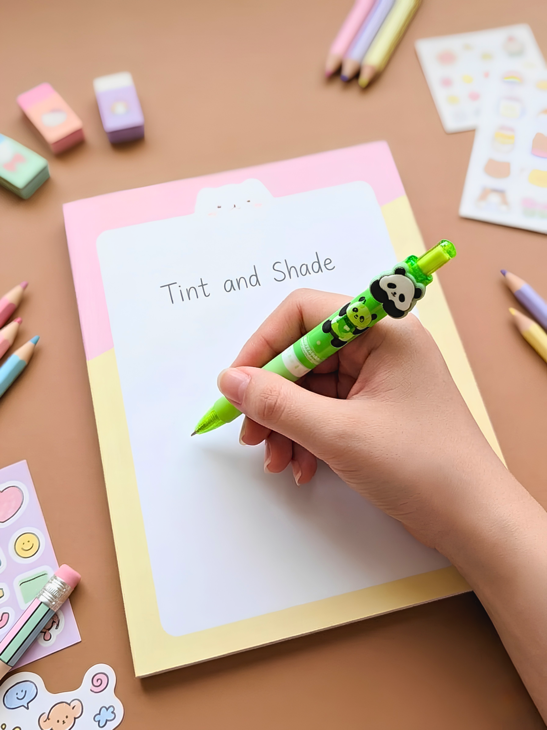 Hand holding a green marker over a piece of paper with 'Tint and Shade' text, surrounded by stationery items on a brown surface.
