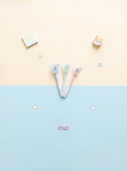Three pens with decorative tops on a two-tone background with stickers.