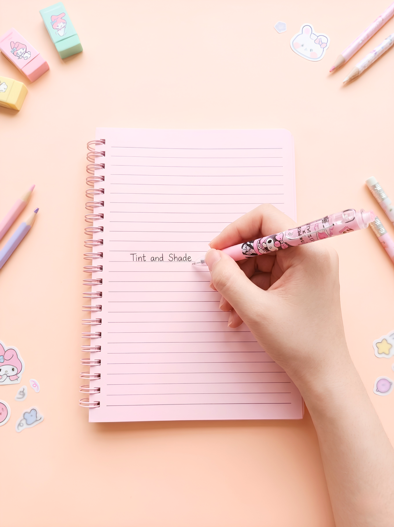 Hand writing in a lined notebook with stationery items on a pastel background