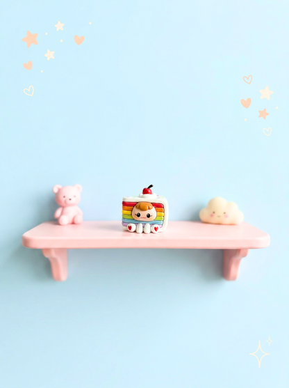 Small pink shelf with a teddy bear, rainbow-colored cloud, and cloud-shaped object against a light blue background.