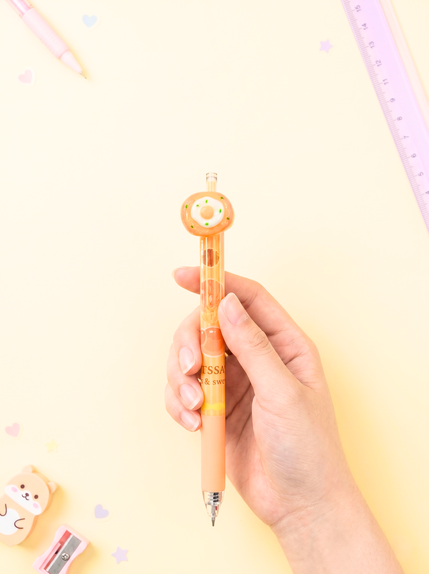 Hand holding a pen with a cute design on a light yellow background