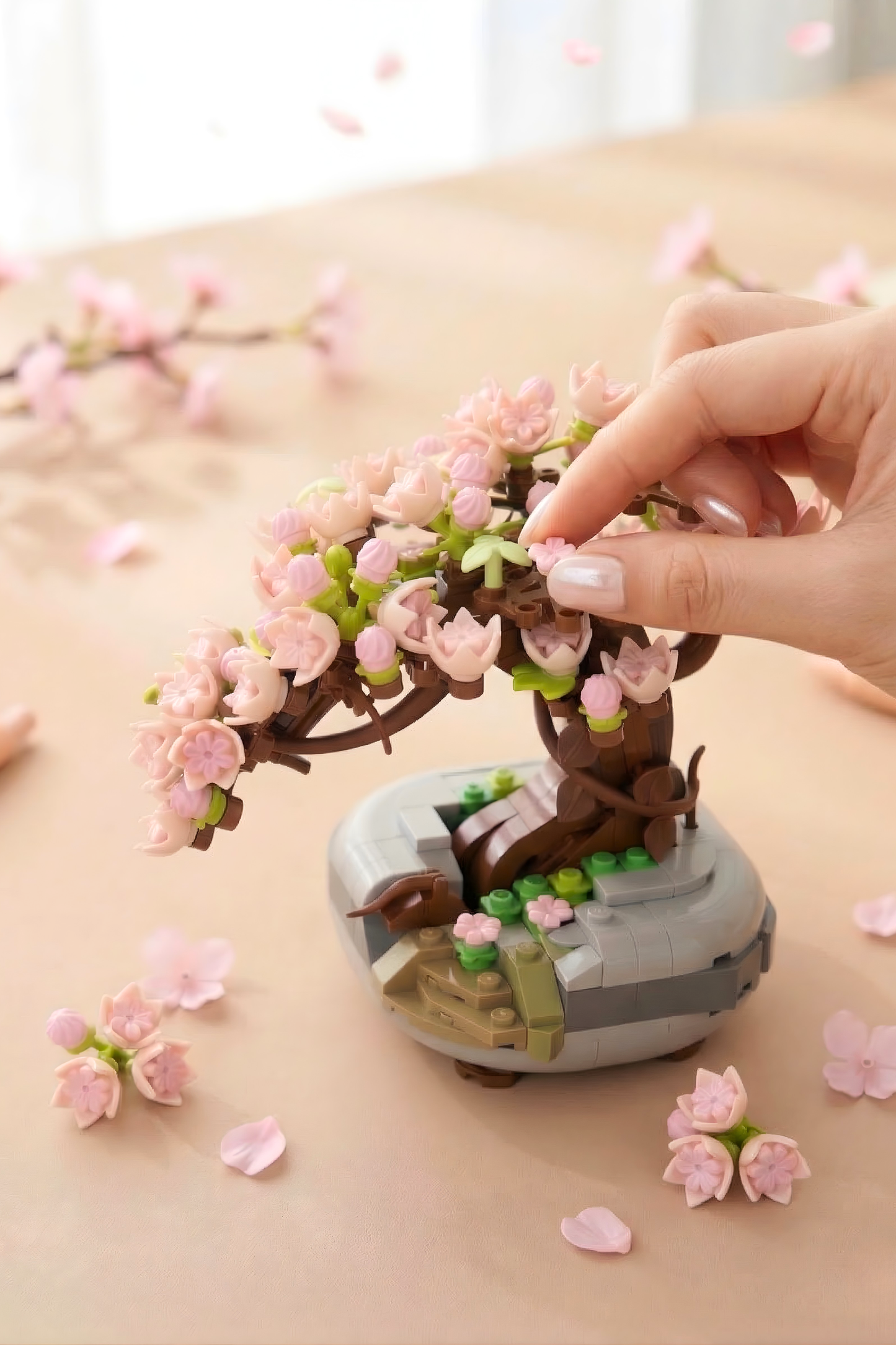 Hand interacting with a small model of a cherry blossom tree on a light surface.