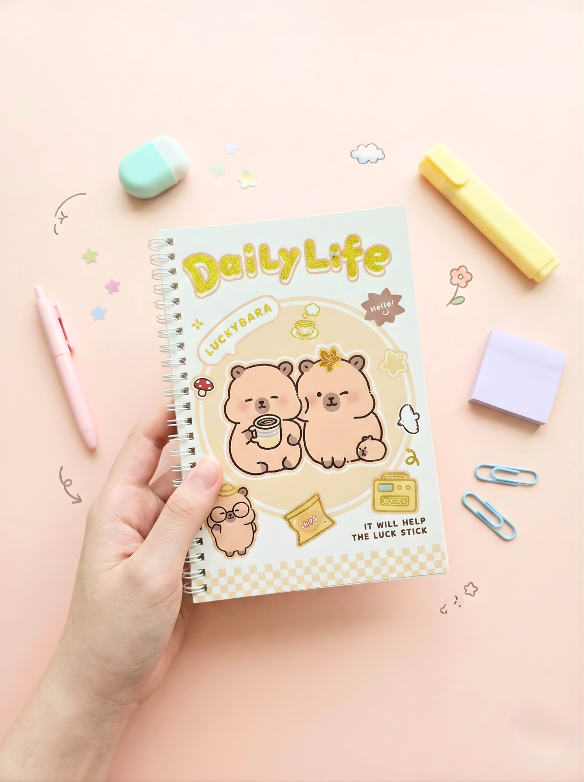 Notebook titled 'Daily Life' held by a hand on a pink background with stationery items.