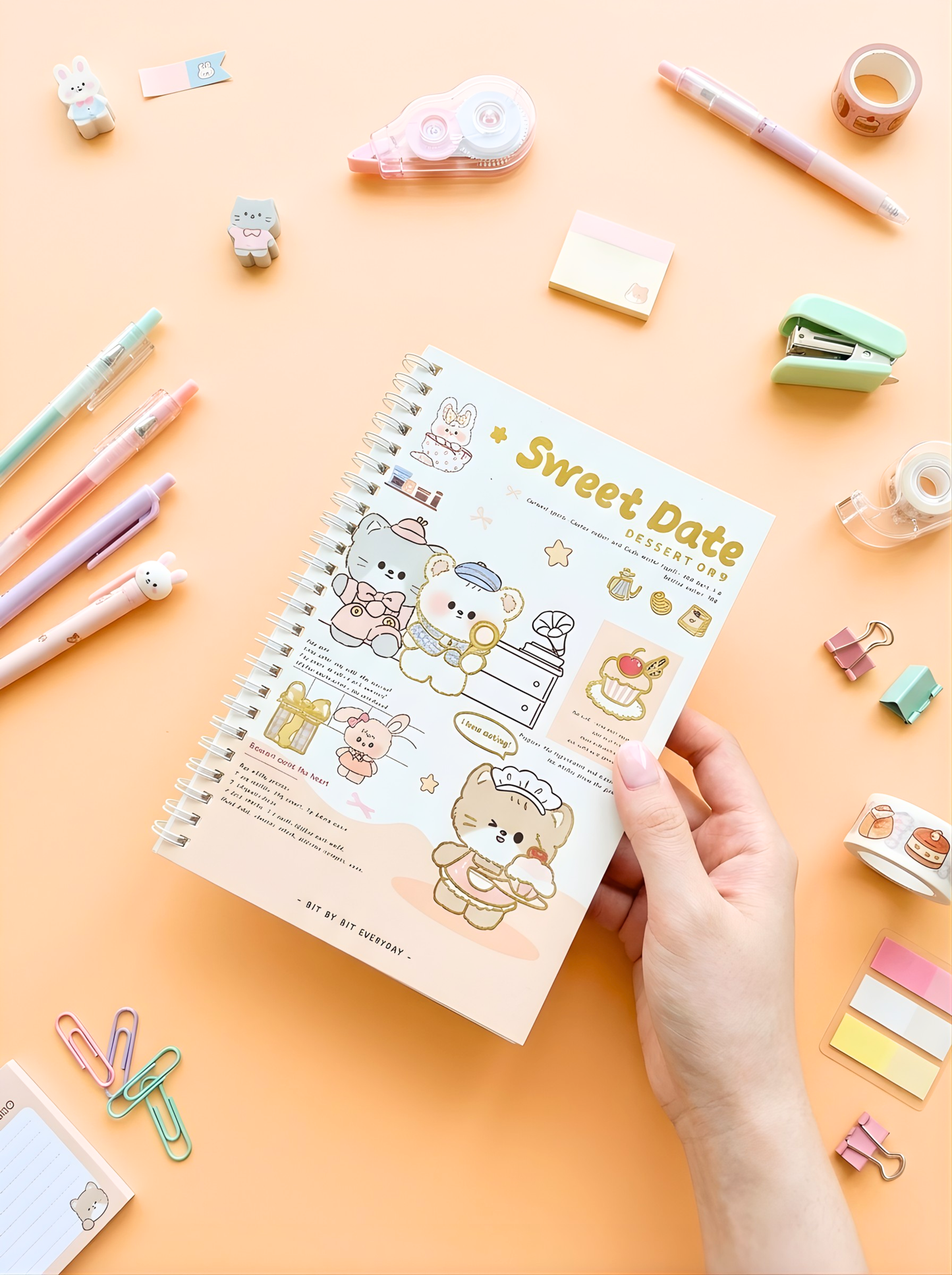 Notebook titled 'Sweet Date' held by a hand with stationery items on a peach background