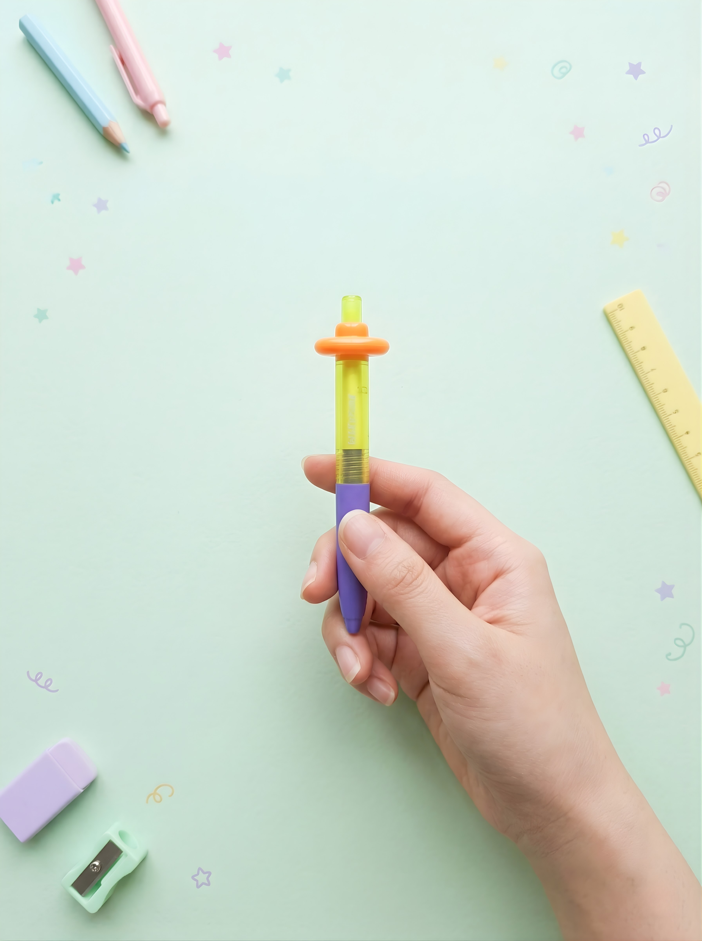 Hand holding a colorful pen with stationery items on a light green background