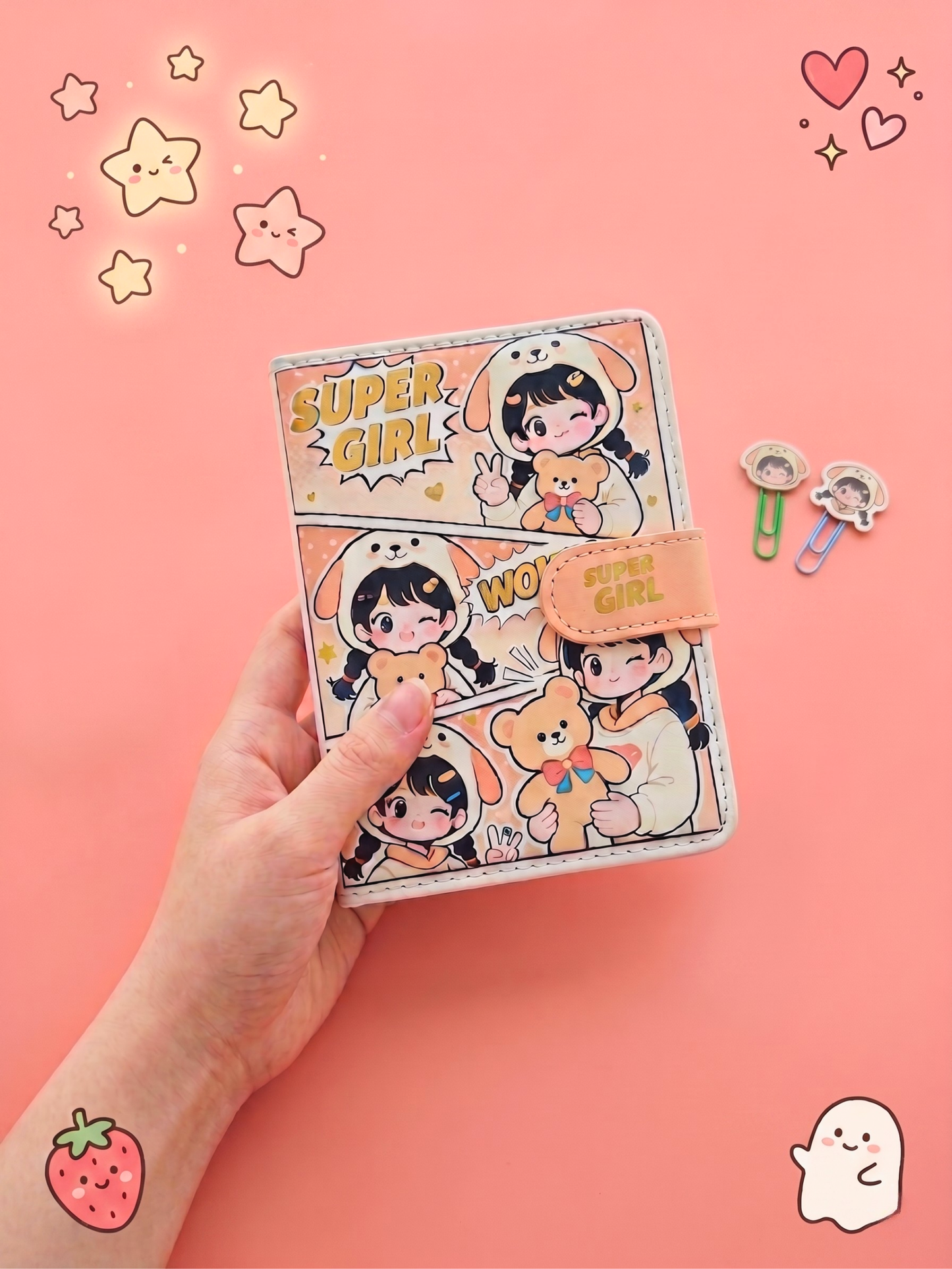 Hand holding a cartoon-themed notebook with decorative elements on a pink background