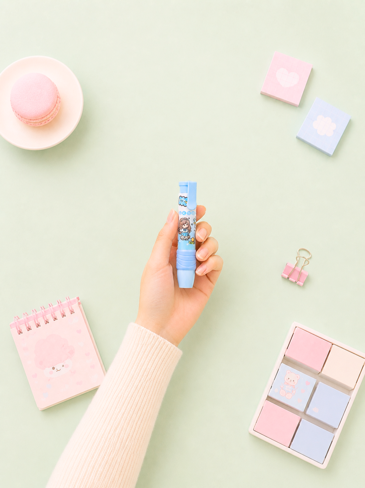 Hand holding a small blue container with stationery items on a light green background
