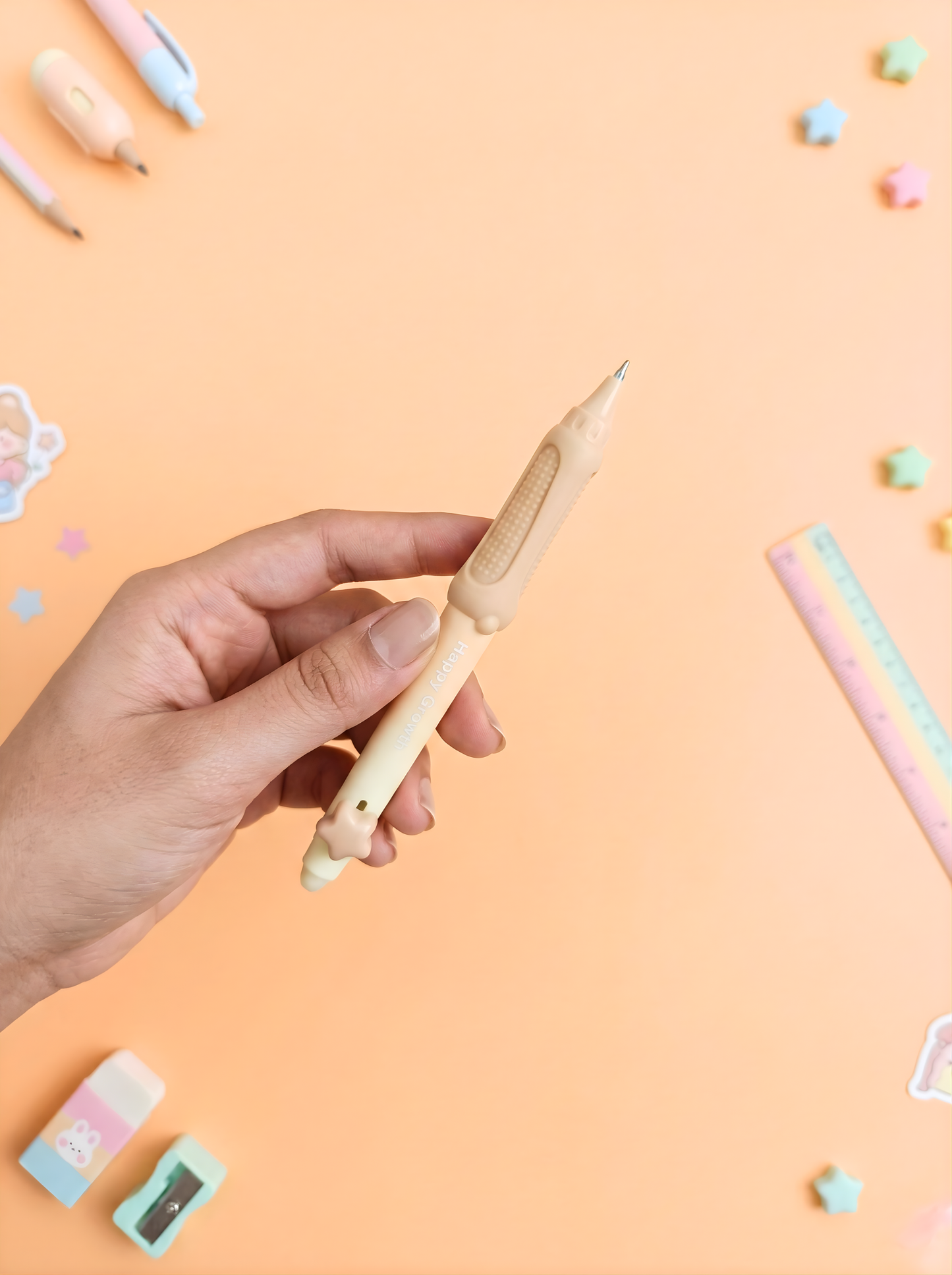Hand holding a wooden pencil on a pastel pink background with stationery items.