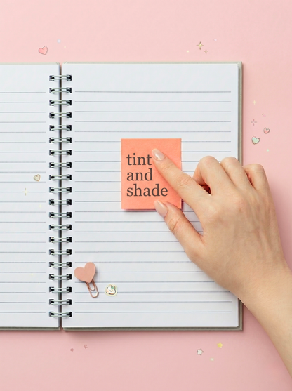 Hand placing a pink sticky note on a spiral-bound notebook with 'tint and shade' text.