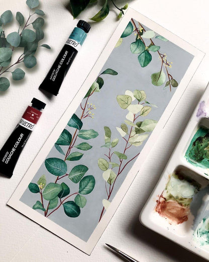 Art supplies including paint tubes and a watercolor painting of leaves on a white surface.