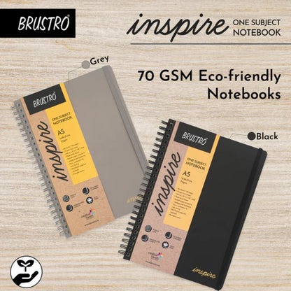 Two Brustro 'inspire' notebooks, one gray and one black, on a wooden surface.